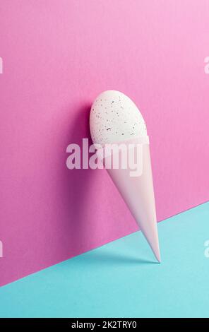 Cono gelato con uovo, sfondo rosa e blu, spazio copia, vacanze di pasqua, stagione estiva, minimalismo e concetto creativo, biglietto di auguri Foto Stock