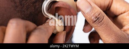 Medico che inserisce il dispositivo di ausilio all'udito nell'orecchio del paziente Foto Stock