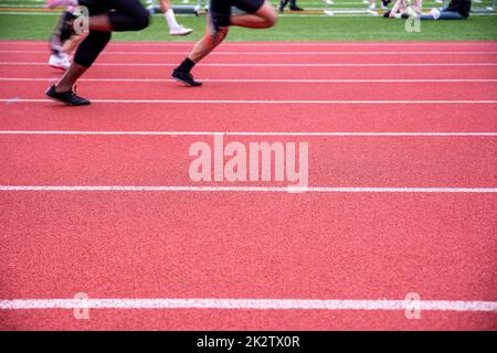 Due corridori corrono su una pista rossa e atletica di campo con marcatori di corsia Foto Stock