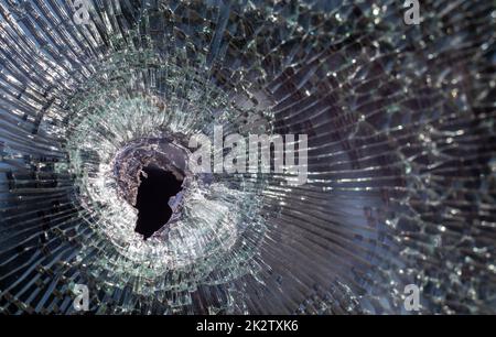 Buco proiettile nel vetro con crepe, primo piano del buco proiettile reale. Scatto autentico. Il proiettile ha creato un foro incrinato nel parabrezza di un'auto o un vetro del finestrino si è rotto a seguito di un incidente. Foto Stock