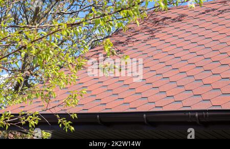 Nuovo tetto con scandole rosse contro il cielo blu. Foto di alta qualità. Tegole sul tetto della casa. Utilizzare per pubblicizzare la fabbricazione e la manutenzione del tetto. Texture macchiata. Copertura conveniente. Foto Stock