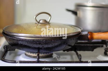 Tostatura di patate fresche in una padella di ghisa con olio di girasole. Una vista su un piano cottura con una padella ripiena di patate fritte dorate in una vera cucina. Cibi cotti in una padella fatta in casa. Foto Stock