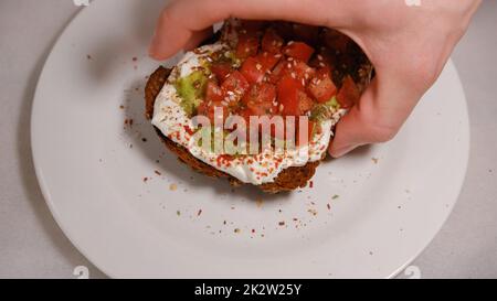 Mano da uomo che taspa i sandwich di avocado, metà di avocado, con arachidi e semi di zucca, tomatos su sfondo bianco Foto Stock
