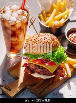 Cheeseburger con manzo, formaggio, pomodori, cipolle e lattuga e un bicchiere di soda ghiacciata e patatine fritte. Foto Stock