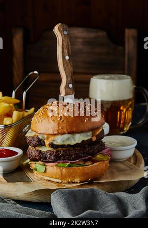 Hamburger di manzo doppio con uova, patate fritte e salse sul tavolo. Foto Stock