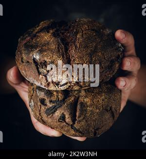 Le mani femminili tengono il pane di segale scuro. Baker con pane fresco su sfondo scuro. Foto Stock