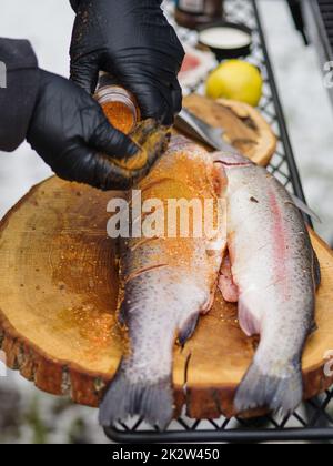 Grillman prepara la trota per grigliare, cosparge le spezie sul pesce. Foto Stock