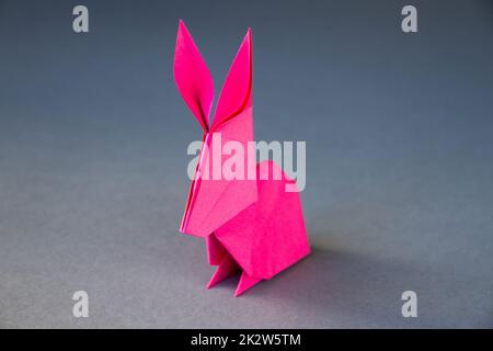 Origami di coniglio di carta rosa isolato su uno sfondo grigio Foto Stock