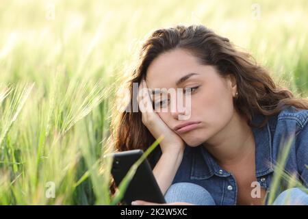 Annoiato donna che controlla il telefono in un campo di grano Foto Stock