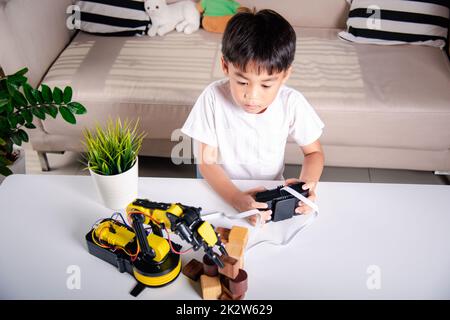 Ragazzo bambino asiatico felice utilizzando il telecomando giocare braccio macchina robotica per raccogliere blocco di legno Foto Stock