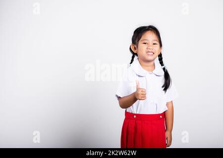 Asian adorable toddler sorridente felice usura studente thai uniforme gonna rossa mostra pollice su dito Foto Stock