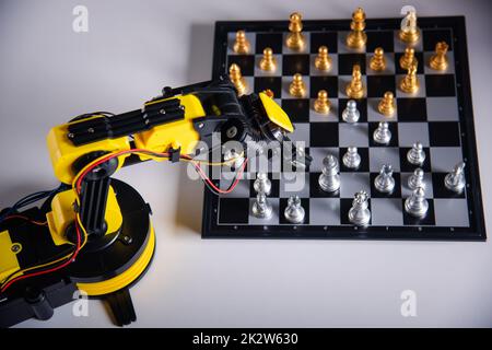 Primo piano braccio robot giallo giocare a scacchi in movimento sulla scacchiera Foto Stock