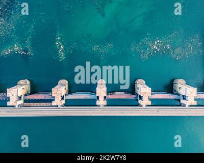 Vista dall'alto della diga, drenaggio dell'acqua attraverso le serrature, banner industriale in blu. Letto di fiume visibile con pietre enormi Foto Stock