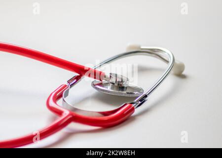 Stetoscopio rosso nell'ufficio medici per il controllo cardio professionale e il controllo del battito cardiaco sano da parte del cardiologo nella sala di trattamento clinico su scrivania bianca come apparecchiatura medica per misurare i parametri del corpo Foto Stock