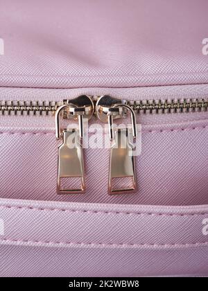 le zip in oro con zip in oro sono fissate su un oggetto in pelle rosa, in primo piano Foto Stock