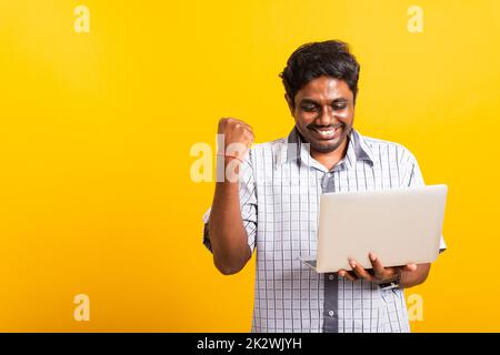 l'uomo nero è eccitato tenendo il computer portatile stringendo pugni e sollevando una mano per il vincitore Foto Stock