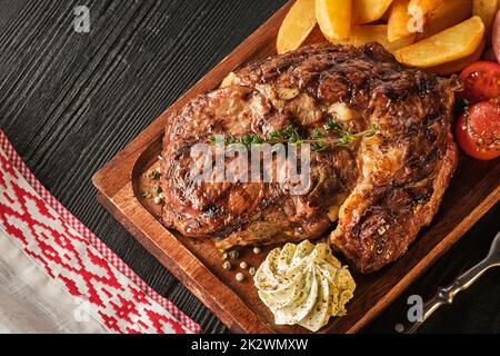 Bistecca Ribeye con patate, cipolle e pomodori ciliegini al forno. Succosa bistecca con burro aromatizzato Foto Stock