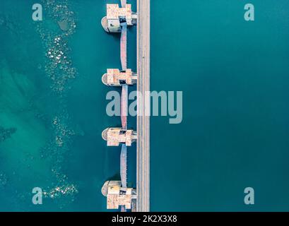 Vista dall'alto della diga, drenaggio dell'acqua attraverso le serrature, banner industriale in blu. Letto di fiume visibile con pietre enormi Foto Stock