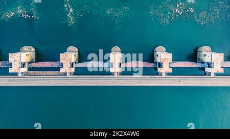 Vista dall'alto della diga, drenaggio dell'acqua attraverso le serrature, banner industriale in blu. Letto di fiume visibile con pietre enormi Foto Stock