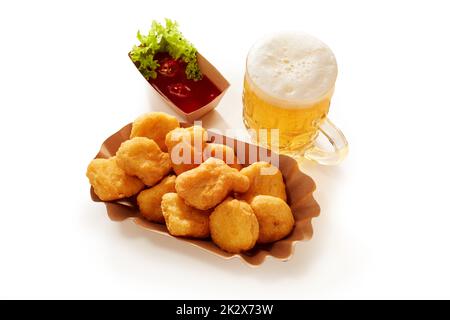 Bicchiere di birra e pepite di pollo sul tavolo Foto Stock