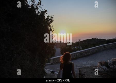 Una donna ha visto camminare lungo i vicoli del villaggio di Pyles durante il tramonto, isola di Karpathos. Karpathos è la seconda isola più grande del complesso greco Dodecaneso, nel Mar Egeo sudorientale. L'isola di Karpathos conserva ancora il suo stile di vita tradizionale, come il villaggio di 'Olympos', dove i nativi indossano ancora i costumi tradizionali. Foto Stock