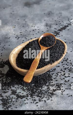 Spezie indiane semi di cumino nero (nigella sativa o kalonji) in ciotola con cucchiaio su tavola di legno primo piano Foto Stock