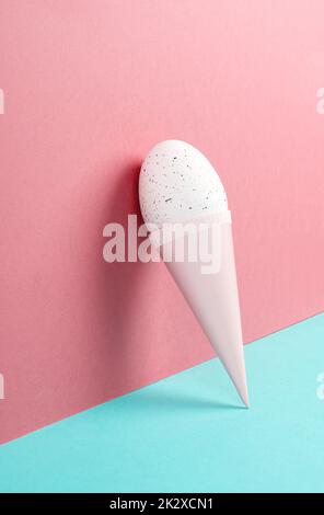 Cono gelato con uovo, sfondo rosa e blu, spazio copia, vacanze di pasqua, stagione estiva, minimalismo e concetto creativo, biglietto di auguri Foto Stock