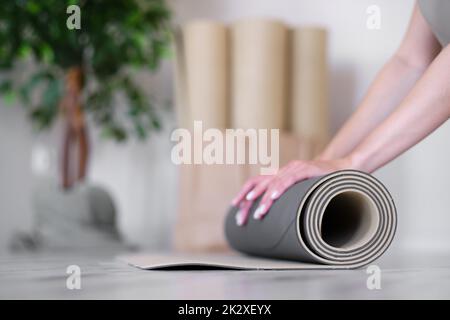 Primo piano delle mani di una donna che rotola su un tappeto per esercizi. Studio yoga. Concetto di uno stile di vita sano. Foto Stock