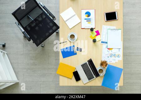 Vista ad alta angolazione della scrivania in ufficio. Computer portatile, tablet, telefono cellulare, carta di credito, caffè, stazionari, documenti, grafici, grafici sono su tavola di legno. Foto Stock