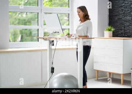 Donna che utilizza una scrivania in piedi ad altezza regolabile in ufficio Foto Stock