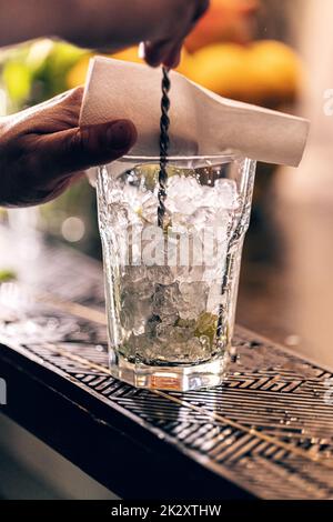 Il processo di preparazione di un cocktail. Barista professionista con una  bottiglia di sciroppo nelle sue mani accanto a un bicchiere di cubetti di  ghiaccio sul bancone del bar Foto stock 