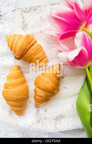 Tre croissant e rosa luminoso tulipani sulla tovaglia di pizzo, close-up Foto Stock