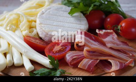 Assortimento di formaggi e fette di pancetta affumicata con erbe e pomodori ciliegini su tagliere di legno Foto Stock