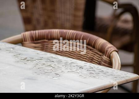 Tavolo vuoto e sedie vuote del ristorante estivo o della birreria all'aperto in estate il giorno piovoso con gocce di pioggia e senza ospiti, non c'è reddito per sedersi sul marciapiede in estate piovosa in ristoranti di blocco pandemic hit Foto Stock