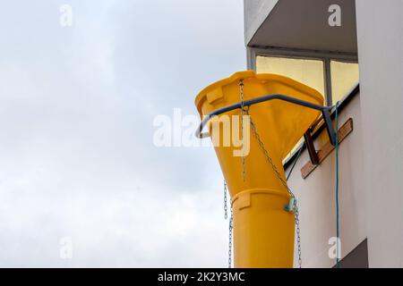 Scivolo di macerie gialle o scivolo di macerie sulla facciata della vecchia casa bianca aiuta con il rinnovamento e la ristrutturazione di vecchie proprietà per la rimozione di macerie pulite e la rimozione dei rifiuti in contenitore per cantiere Foto Stock