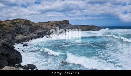 Un mare con forte rigonfiamento che batte contro le pareti di una scogliera rocciosa, mare azzurro con grandi onde con schiume che si schiantano contro le rocce, Minorca, Spagna Foto Stock