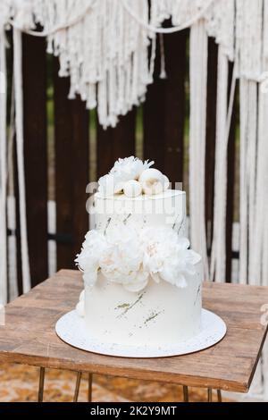 Torta nuziale in stile boho. Dolci di nozze. Elegante torta nuziale bianca con fiori e sfere di cioccolato bianco Foto Stock