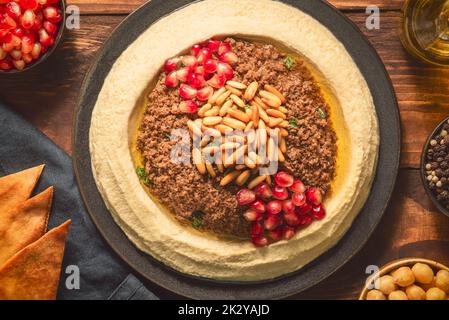 Cucina araba; tradizionale salsa cremosa di hummus con macinato di manzo. Condito con olio d'oliva, semi di melograno freschi, pinoli tostati e prezzemolo. Foto Stock