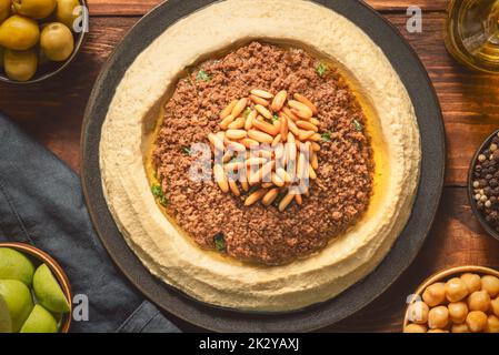 Cucina araba; tradizionale salsa cremosa di hummus con macinato di manzo. Condite con olio d'oliva, pinoli tostati e prezzemolo. Vista dall'alto con primo piano. Foto Stock