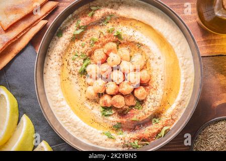 Cucina araba; hummus cremoso tradizionale in ciotola scura. Condito con olio d'oliva, paprika, ceci cotti speziati e prezzemolo. Foto Stock