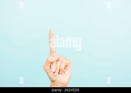 La mano femmina mostra il numero uno. Donna che punta verso l'alto con l'indice su sfondo azzurro Foto Stock