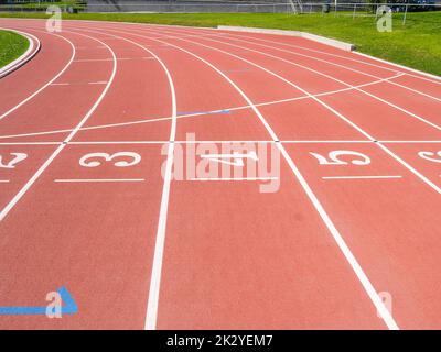 Corsie numerate bianche sulla pista da corsa sintetica rossa Foto Stock