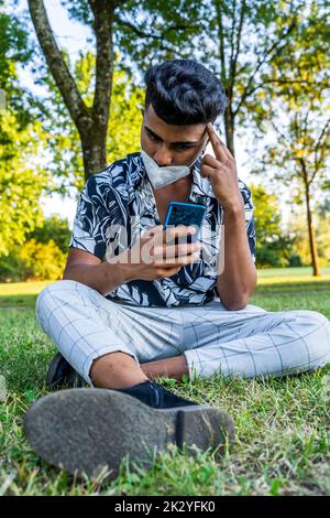 giovane bell'uomo che usa lo smartphone all'aperto indossando una maschera anti-contagio durante l'emergenza covid-19 Foto Stock