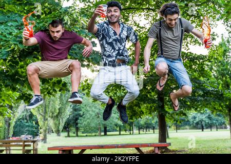 gruppo di millenni che si divertono a saltare mentre si bevono cocktail colorati all'aperto Foto Stock