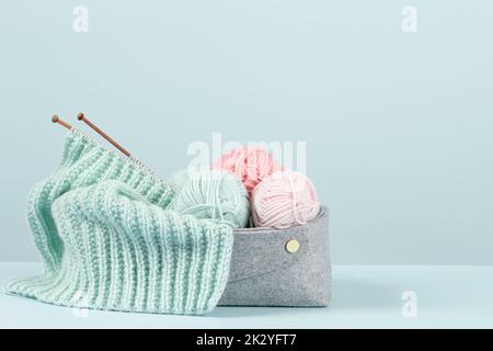 Sfondo Unione. Filo da maglieria, aghi di bambù e maglione a maglia nuovo in basket su sfondo azzurro. Hobby fatto a mano, relax a. Foto Stock