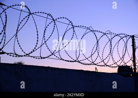 Recinzione con filo spinato sfondo cielo durante il tramonto Foto Stock