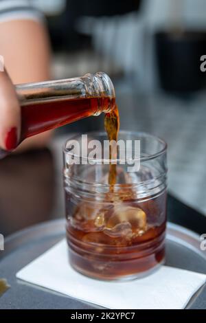 Versare il caffè freddo preparato in una tazza di vetro con cubetti di ghiaccio, caffè preparato Foto Stock