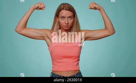 Sono forte e indipendente. Donna che mostra bicipiti, guardando fiducioso, sentire forza di potere per combattere per i diritti, energia per ottenere successo vincere. Giovane ragazza adulta isolata su sfondo blu parete studio Foto Stock