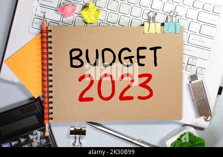 Su sfondo rosa, relazioni, graffette nere, occhiali e un notebook bianco con il budget di testo 2023. Foto Stock