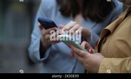 Primo piano concentrarsi sulle mani delle donne utilizzando i telefoni. Due donne con smartphone per strada, la ragazza spiega, mostra, racconta, dimostra, gesticulates Foto Stock